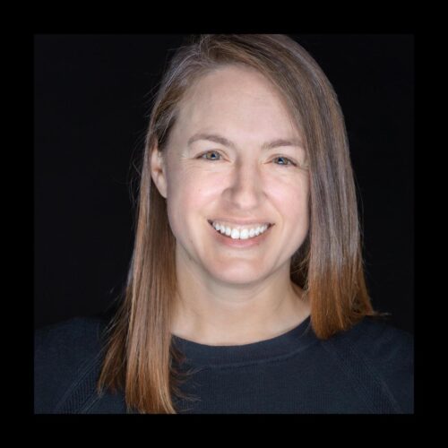 white complexion woman smiling, chest length hair, right ear showing, blue shirt