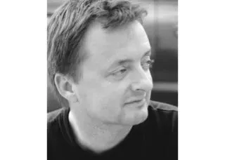 man with short hair black tshirt looking to his left as camera photographs, picture is black and white