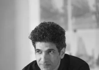 man in orange shirt black skin arms crossed looking focused at the camera