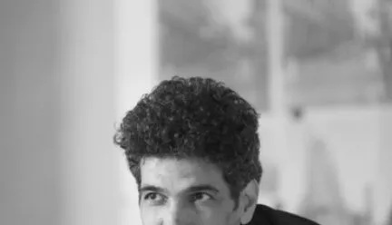 man in orange shirt black skin arms crossed looking focused at the camera