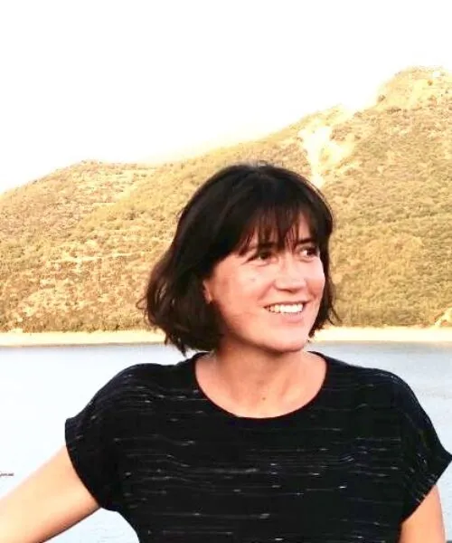 woman smiling to the right tan complexion black hair black tshirt in front of mountain