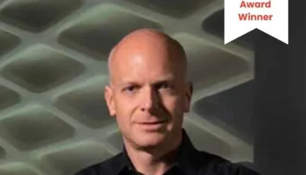 bald man black shirt arms crossed staring at camera