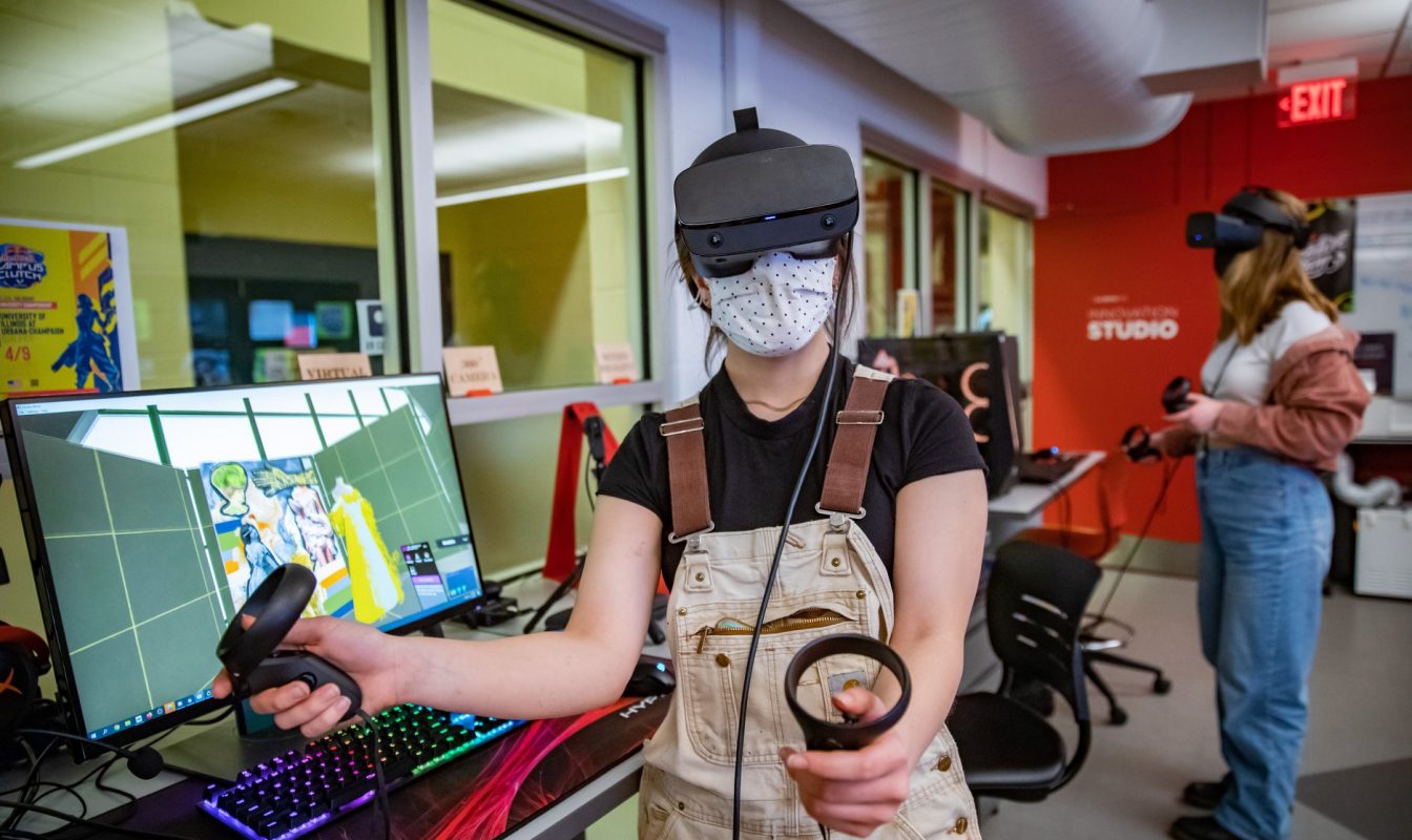 Photo of two students using VR headsets and hand held controllers in a computer lab