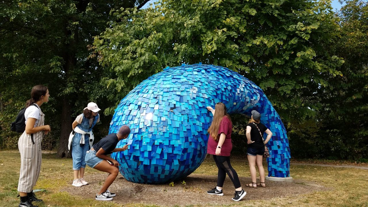 Students gathered around a large blue outdoor sculpture.