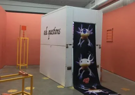 Photo of an art installation with a booth labeled "ask questions"