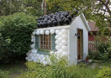 Photo of a small white house with black and white balls on the wall and roof