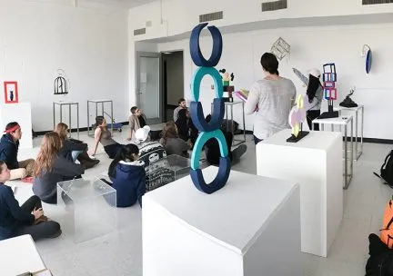 Photo of students sitting cross legged in an art gallery discussing the work