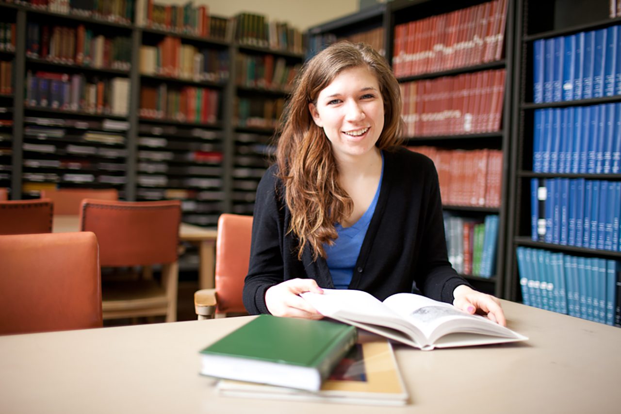 Smiling student with books at a library table