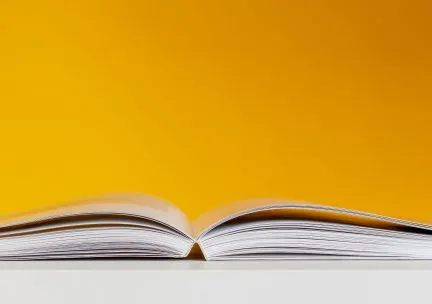 Eye level photo of an open book with a bright yellow background.