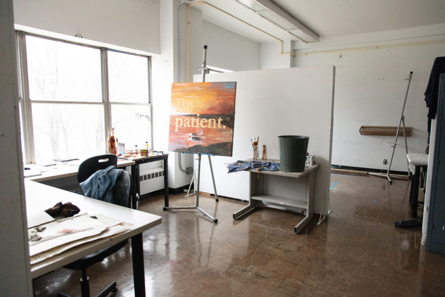 painting on sunset reading "be patient" in front of a white studio wall