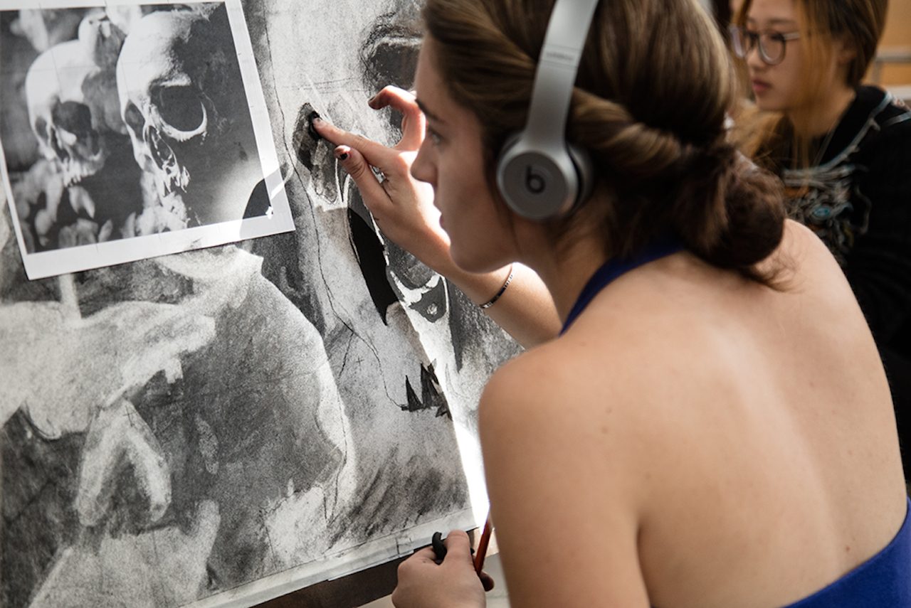 Photo of a student working on a charcoal drawing at an easel