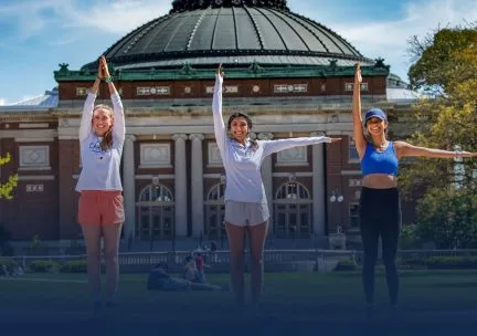 Photo of students posing with arms upraised in front of Foellinger Auditorium on the South Quad