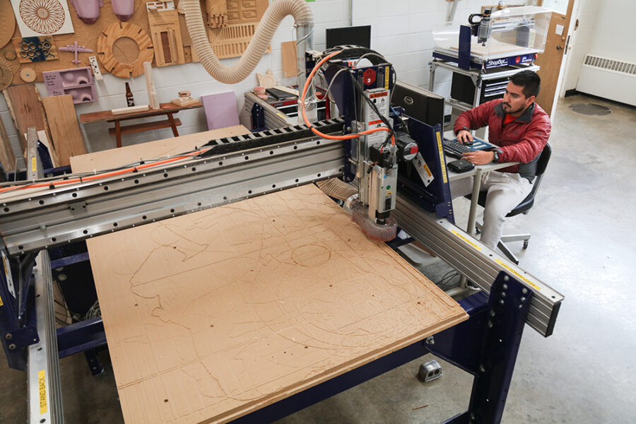 student prepares file at a computer in front of a CNC router