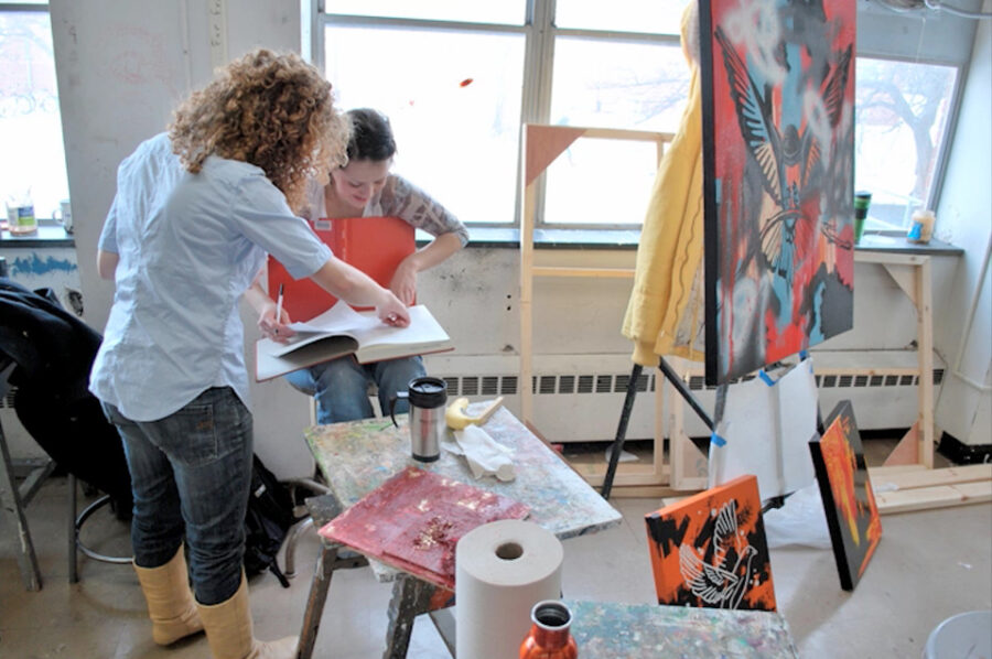 students looking at sketchbook near large painting