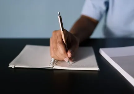 Closeup photo of a hand writing with a pen in a notebook