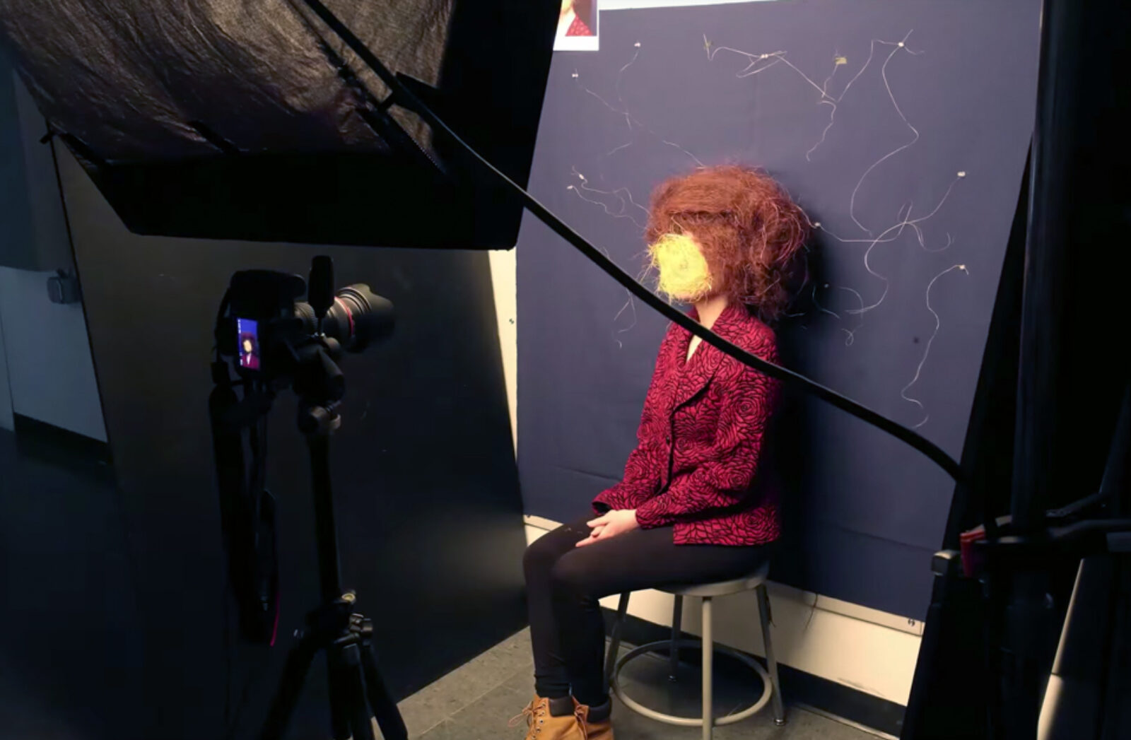 student sits for portrait in photography studio, face is obscured by yellow thread