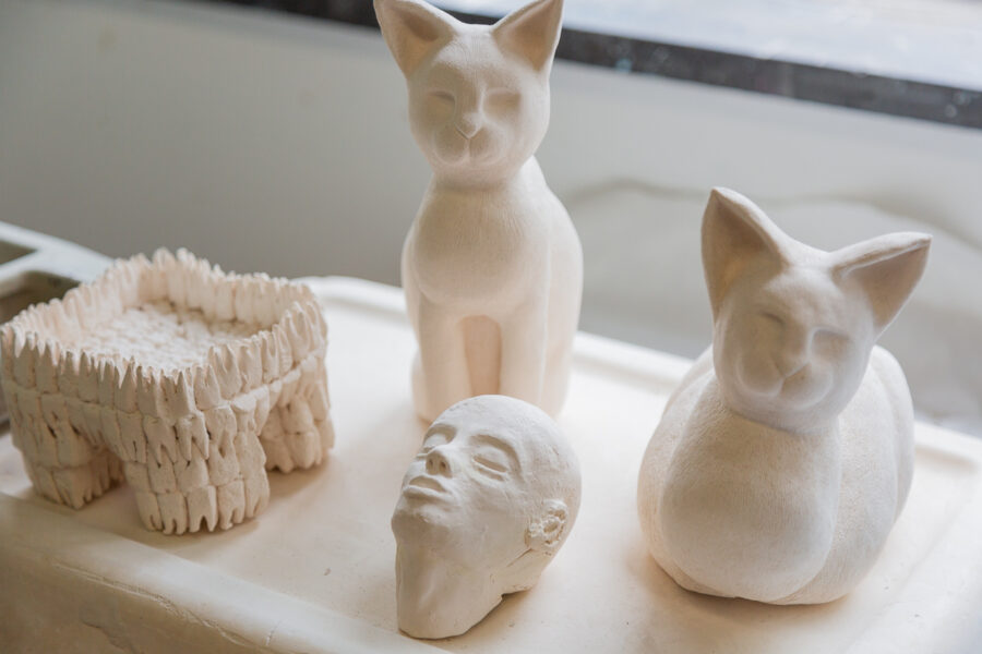 photo of two ceramic cat sculptures, a sculpted human head, and stool made out of ceramic teeth