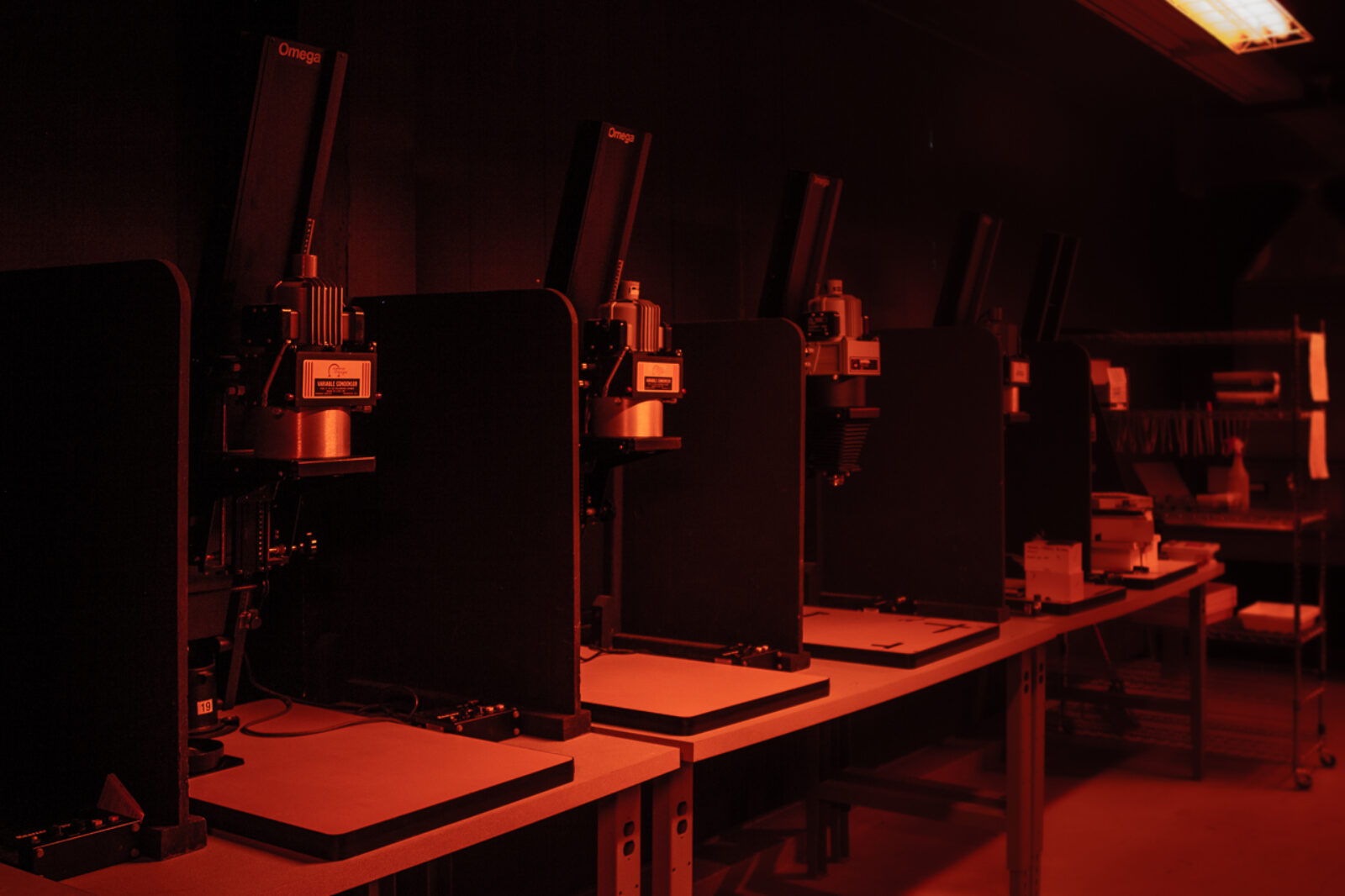 row of enlargers in darkroom under red safe lights