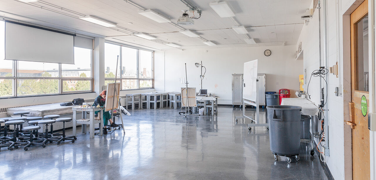 photo of a large room with stools, easels, and a student painting on a canvas