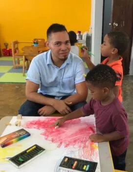 art teacher smiling, sitting with two students drawing