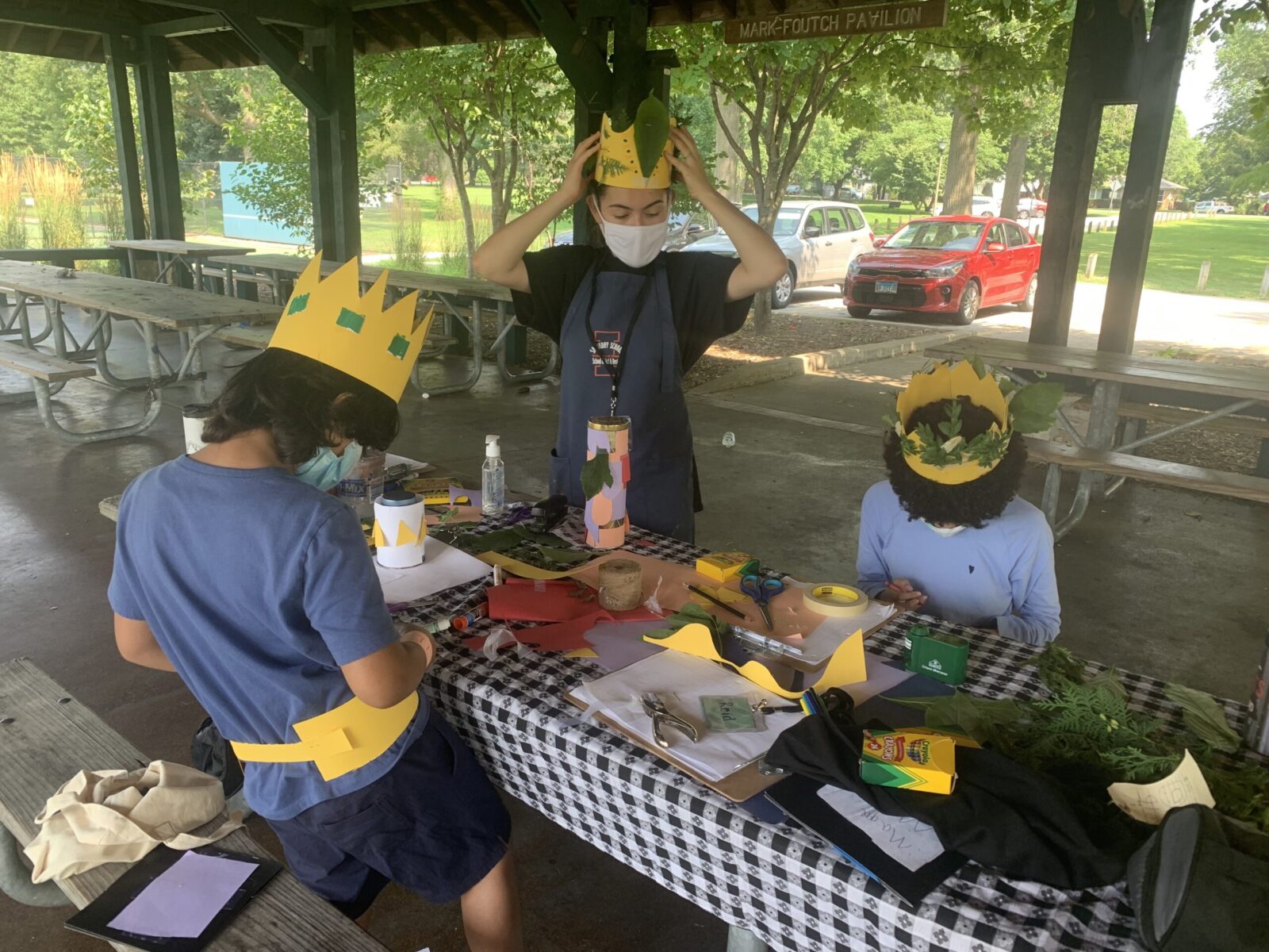 An art teacher shows their students how to make paper crowns and decorate them with fallen leaves and branches