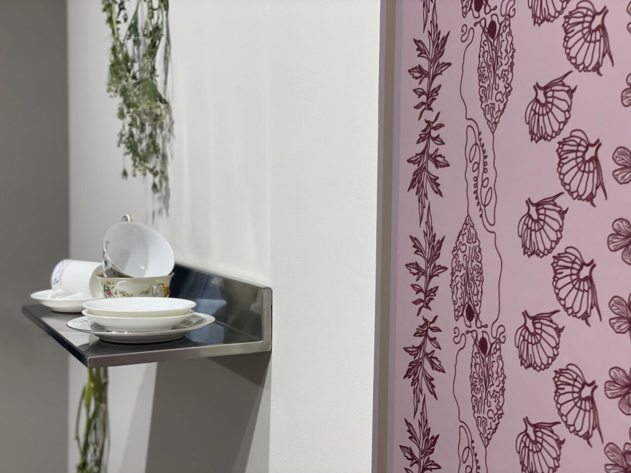 Image of an installation consisting of pink wallpaper with floral patterns and a shelf holding pieces of china.