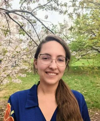 lindsey stirek wearing a blue dress standing in front of a blooming tree