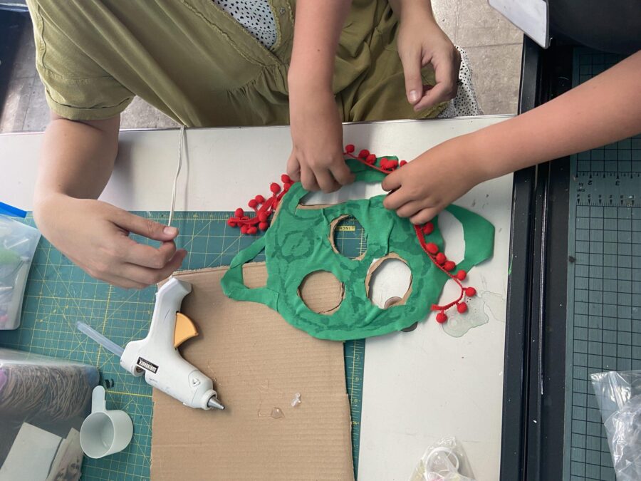 a teacher helping a child glue tassels to their mask