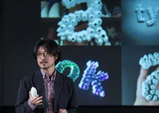Lee giving a lecture with photos of work in background