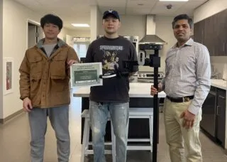 3 people standing in a lab, two hold a certificate