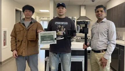 3 people standing in a lab, two hold a certificate