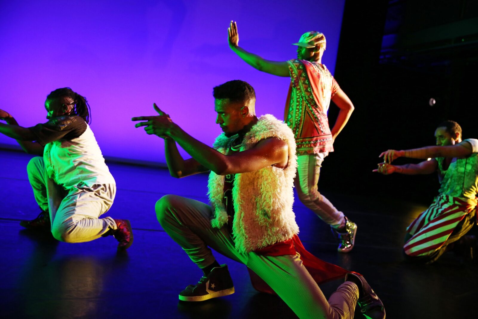 Three dancers hover on the floor as another dancer stands behind them, reaching out with their arm