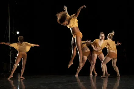 One Dancer in midair with arms up and other dancers on the floor