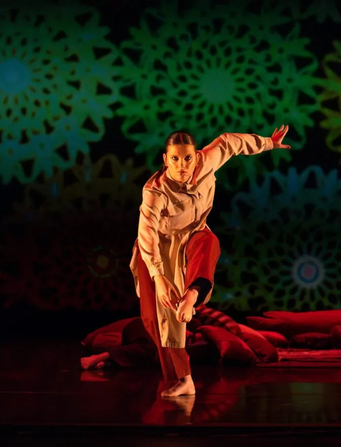 A lone dancer reaches their right arm forward in front of a green scrim