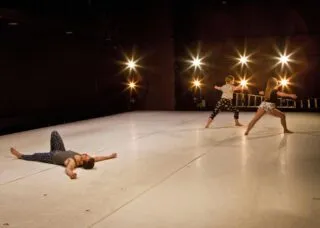 dancer on the floor with two other dancers standing in the corner