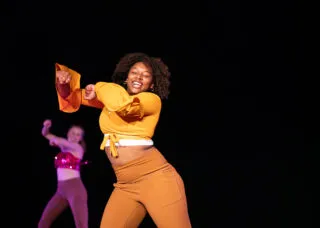 a dancer dressed in orange throws her arms up and sways