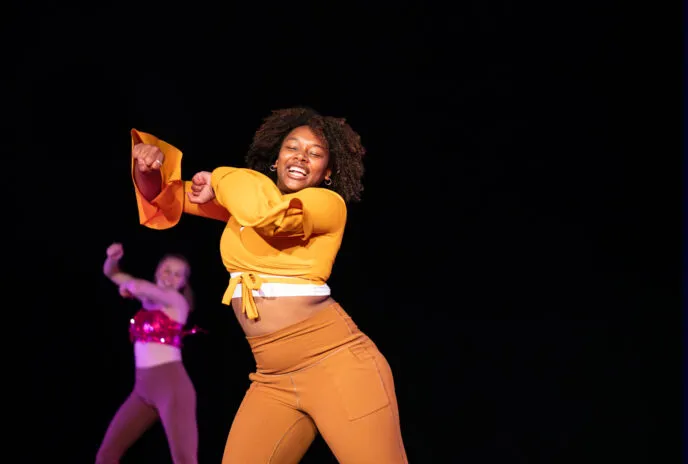 a dancer dressed in orange throws her arms up and sways