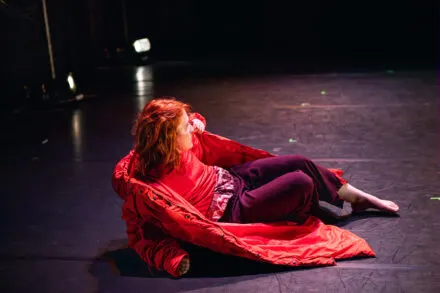 A dancer lies on the floor with a red coat