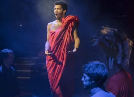 Person in toga standing in shaft of light during theatre production