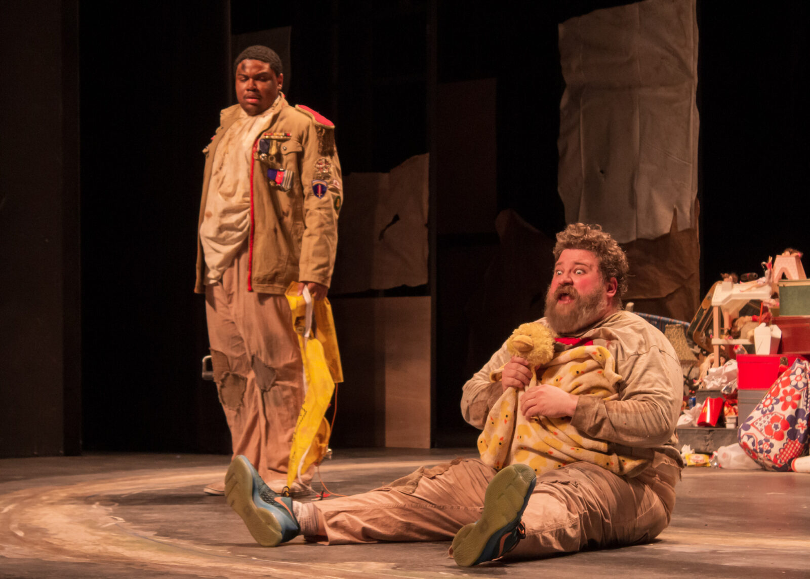 Actor sitting on stage with actor looking on