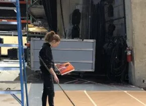 a person holds a painting and stands above a large canvas tracing out the design