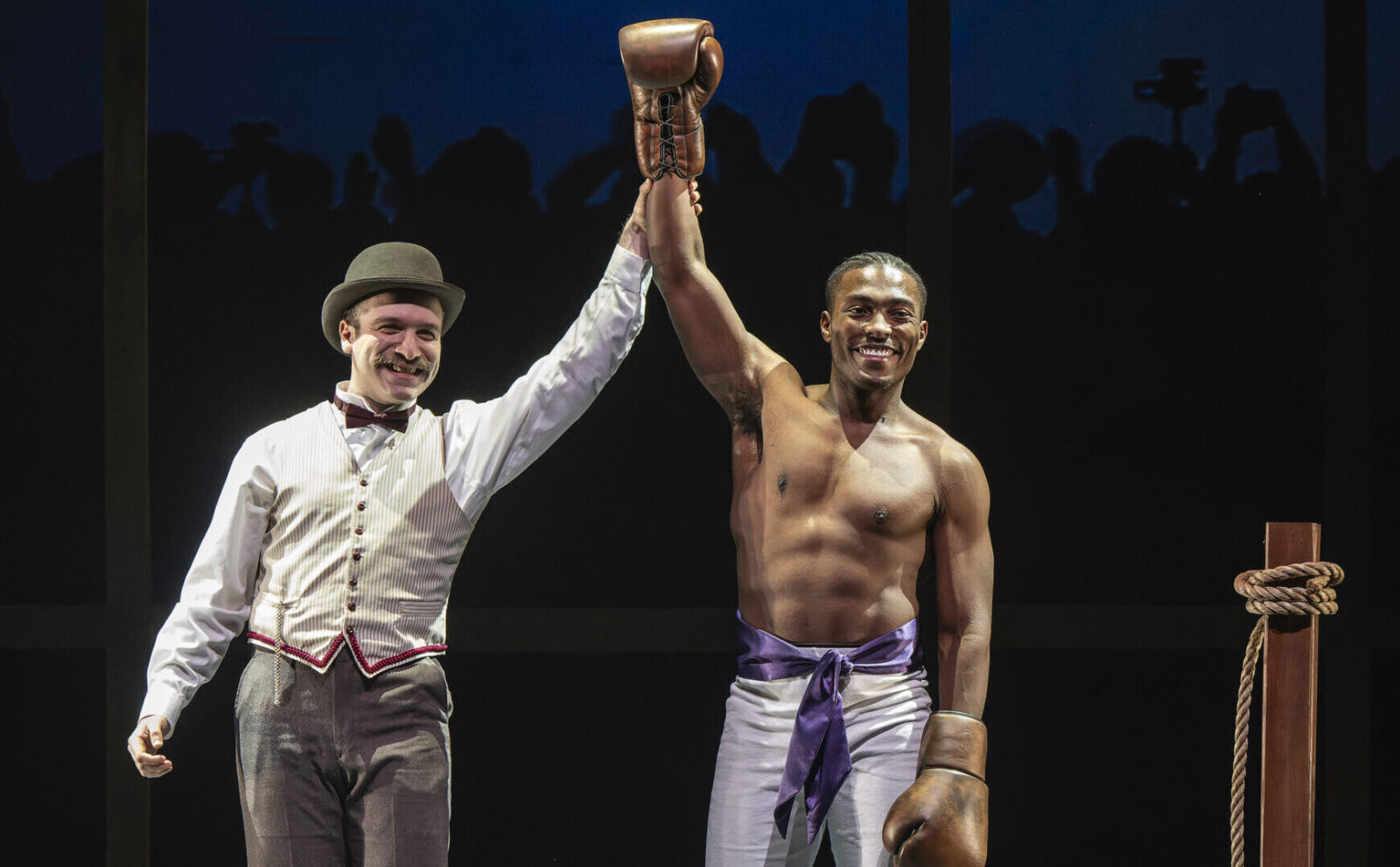 Two actors engage onstage in Roman costumes. One gestures toward the audience.