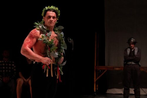 person shirtless with garland wreath on head and around shoulders