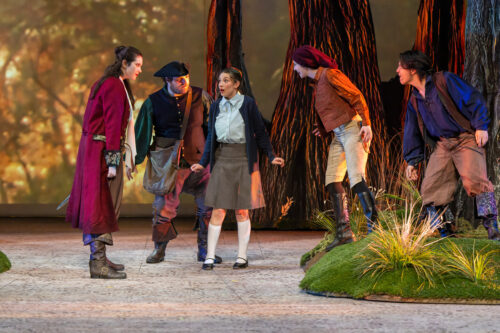 actors onstage with bright lights and scenic trees