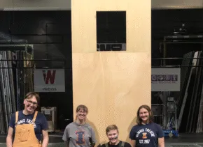 people smiling standing in front of a large wooden dumbwaiter