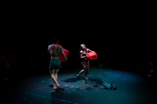2 people onstage in blackbox theatre spilling gasoline