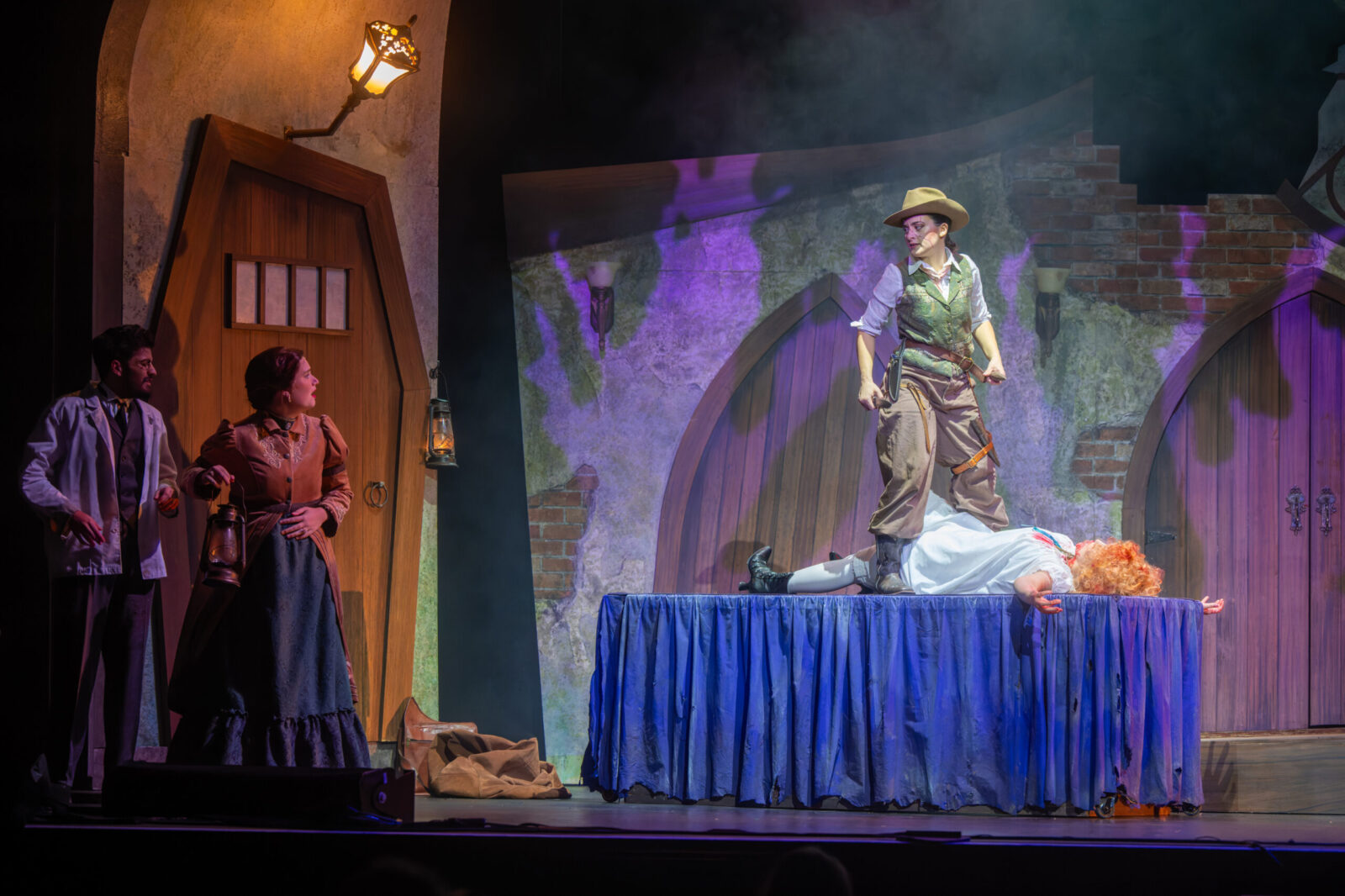 person onstage stands on table over person pretending to be dead