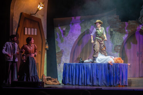 person onstage stands on table over person pretending to be dead