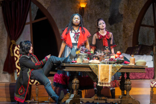 3 people onstage around a large dining table