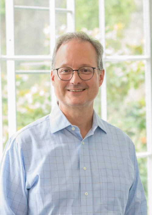 Man in blue shirt and glasses smiling in front of window